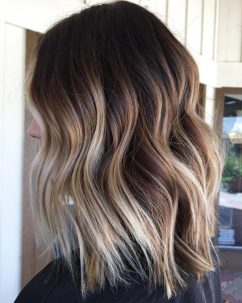 Cheveux avec balayage à fort contraste entre racine foncée et longueurs blondes, de profil