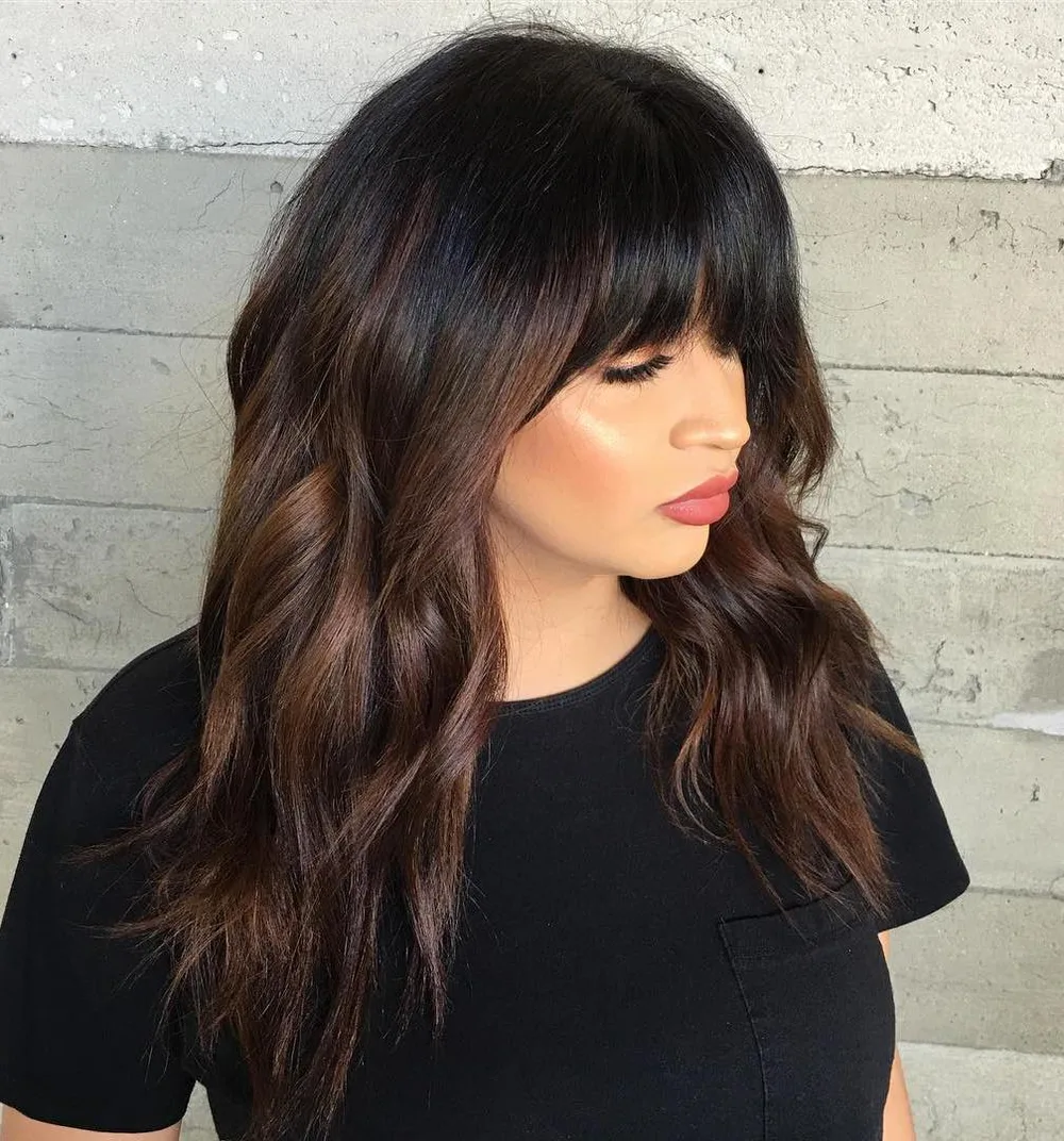 Cheveux bruns avec balayage caramel et frange, longueurs ondulées, de face