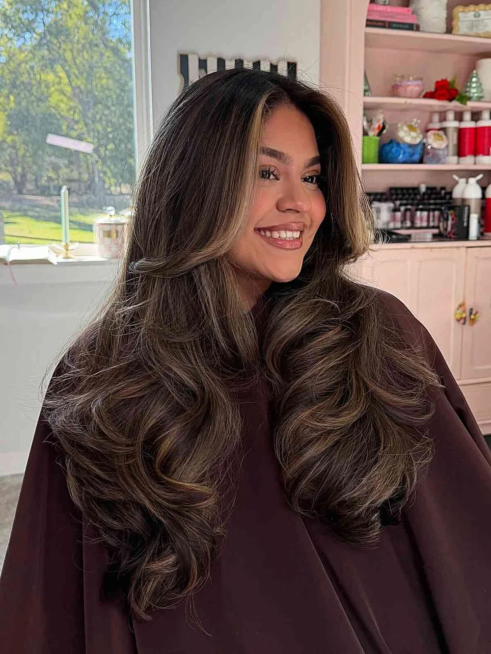Cheveux chocolat riche parsemés de reflets caramel, mi-longs ondulés