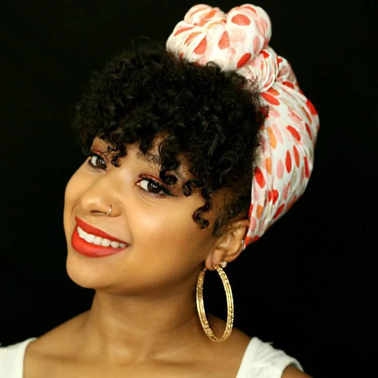 Femme aux cheveux crépus portant un afro avec un foulard coloré noué, de face souriante