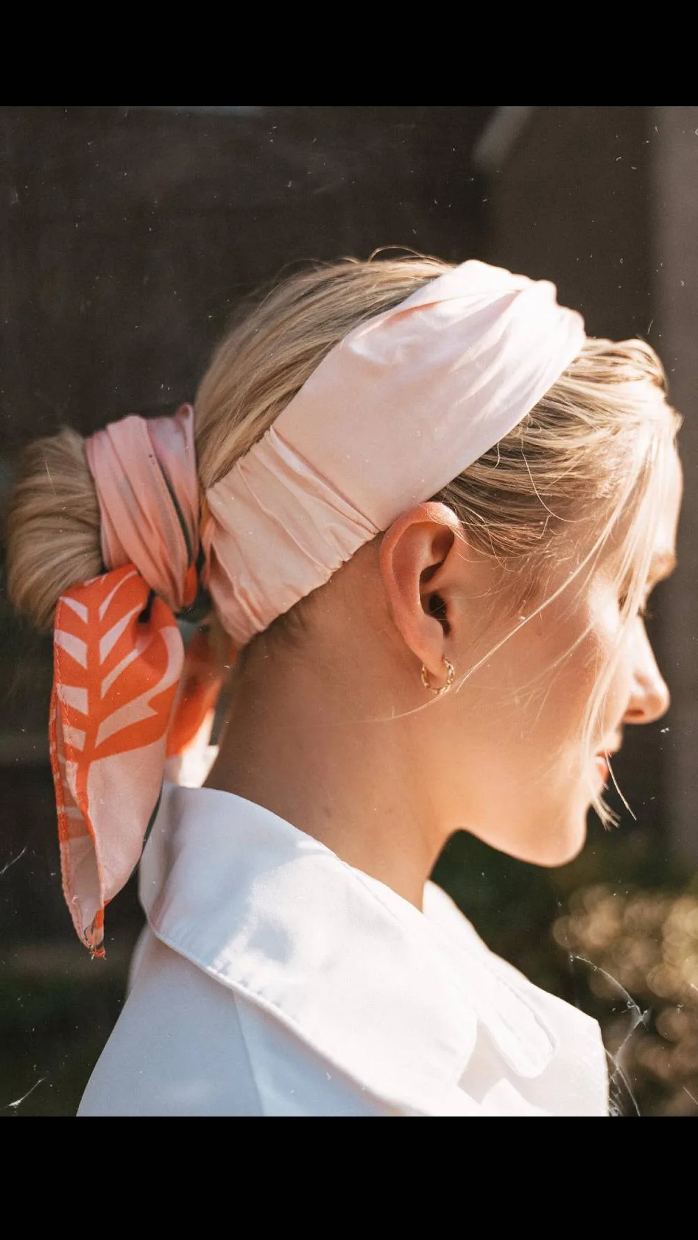 Femme blonde avec un foulard orange noué en bandeau dans les cheveux, de dos
