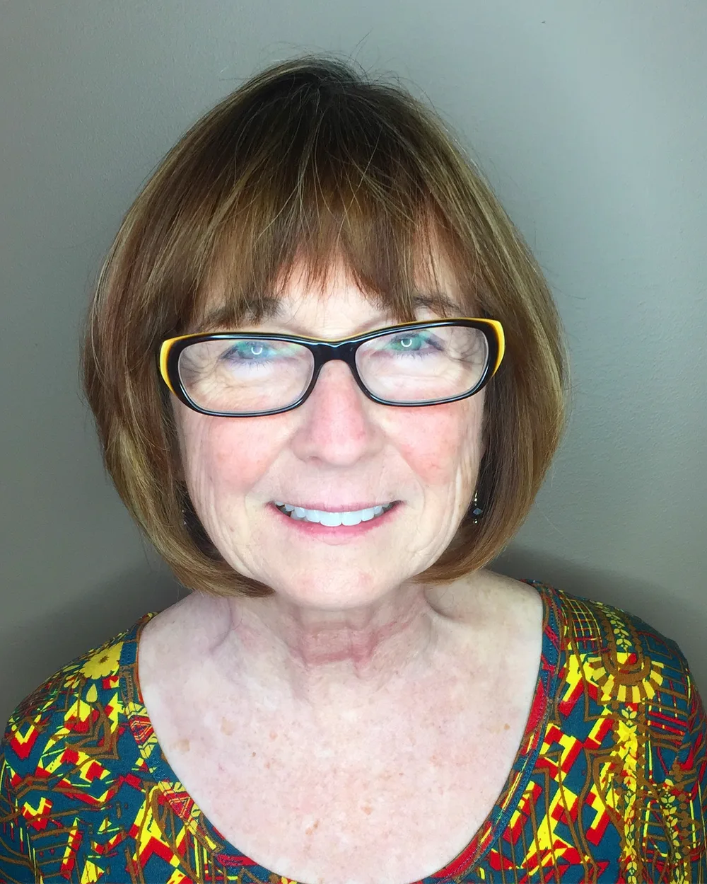 Femme de 70 ans avec carré brun et frange pleine, lunettes, de face