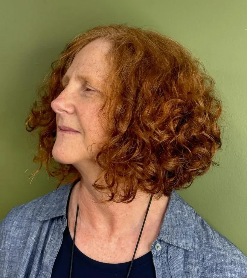 Femme de 70 ans avec crop court bouclé auburn cuivré, de profil