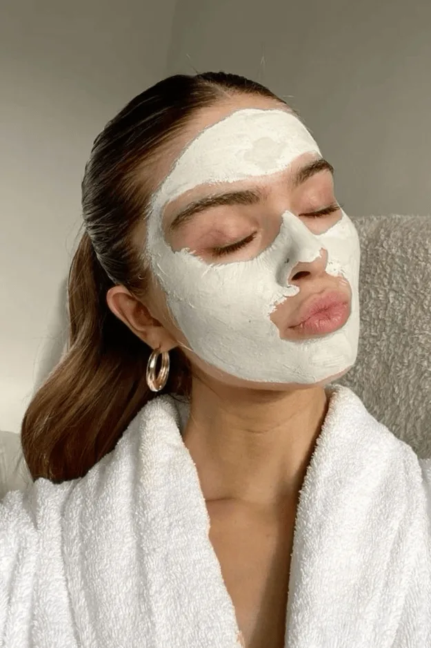 Femme en peignoir portant un masque à l'argile verte sur le visage