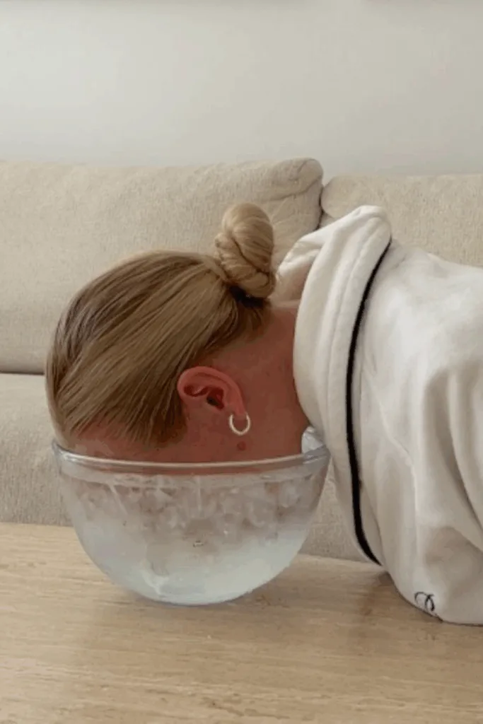 Femme plongeant son visage dans un bol d'eau glacée posé sur une table