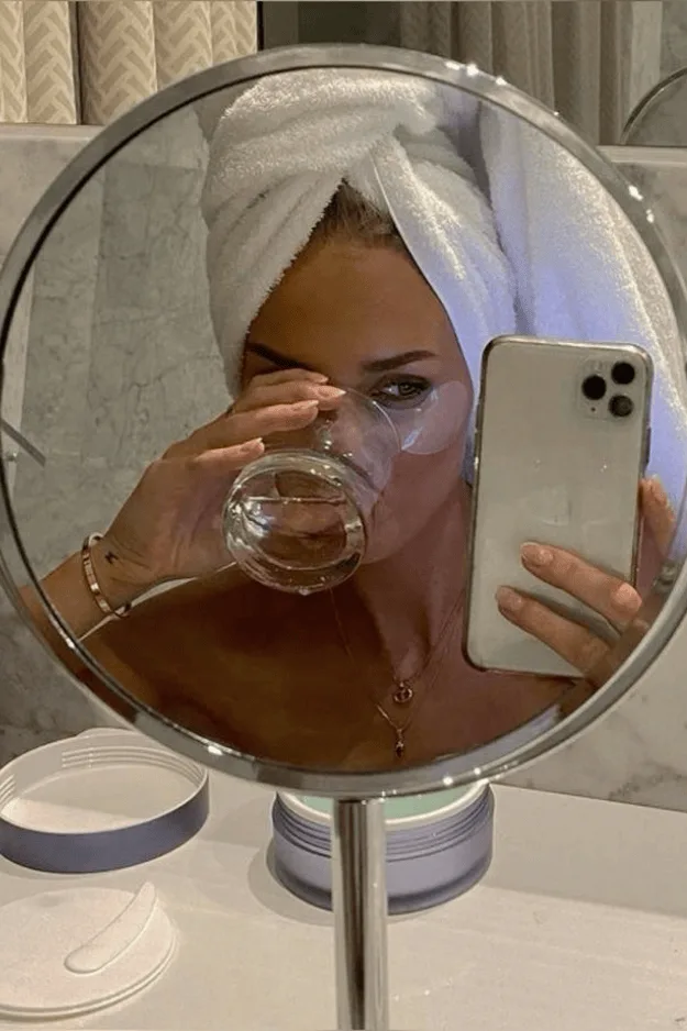 Femme se regardant dans un miroir grossissant rond, verre d'eau à la main