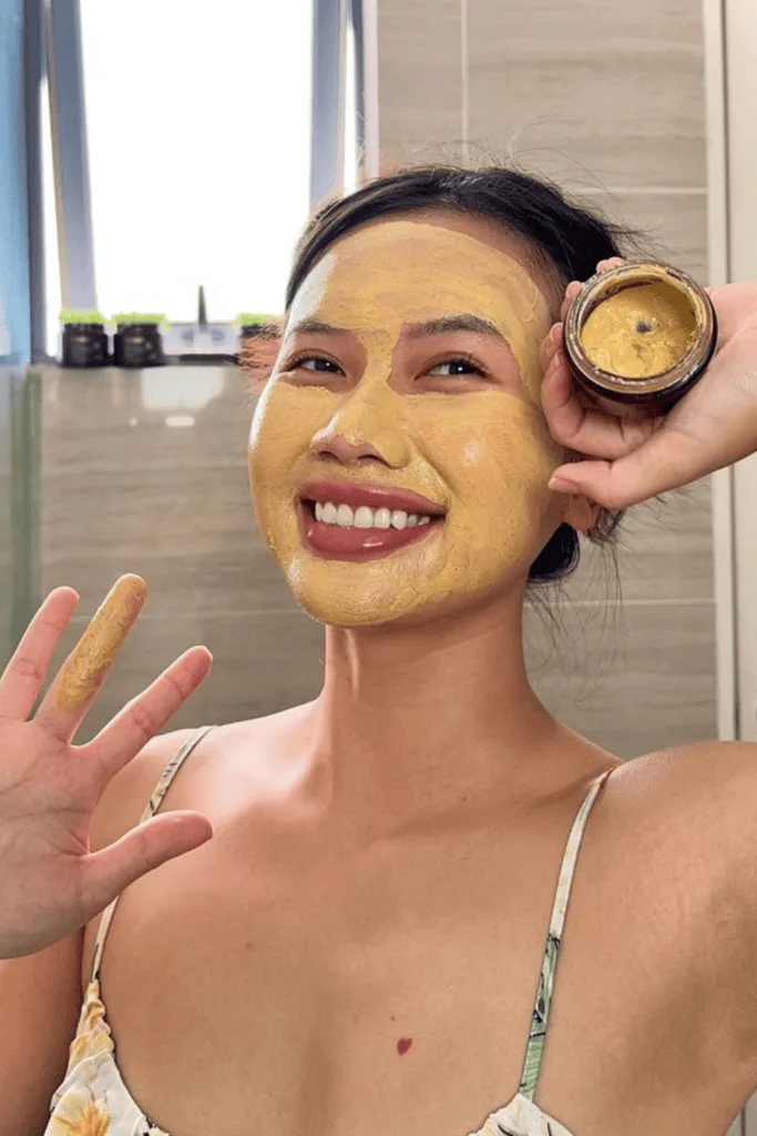 Femme souriante au teint lumineux portant un masque au curcuma jaune