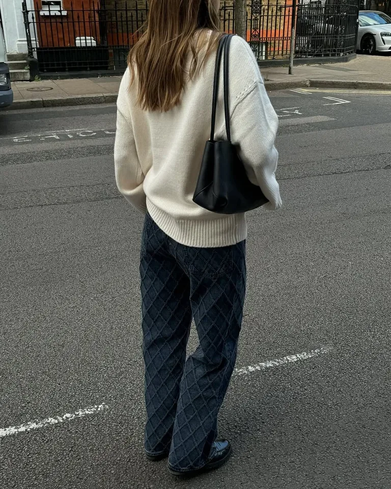 Jean brut large porté avec un pull crème ample et un sac noir