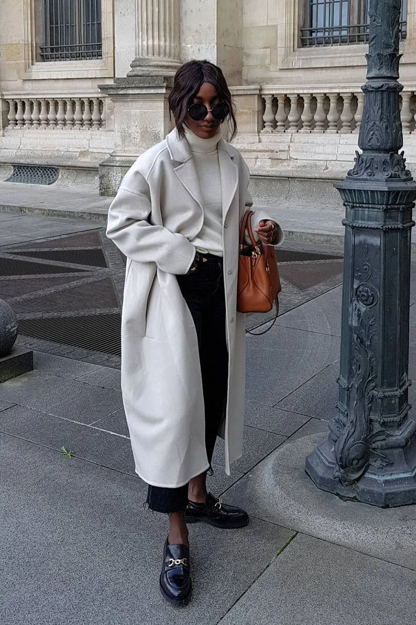 Jean noir avec manteau long gris clair, mocassins noirs et sac marron