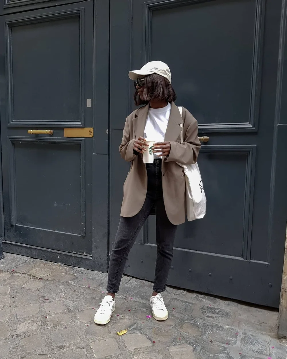 Jean noir droit avec blazer taupe, casquette blanche et baskets blanches