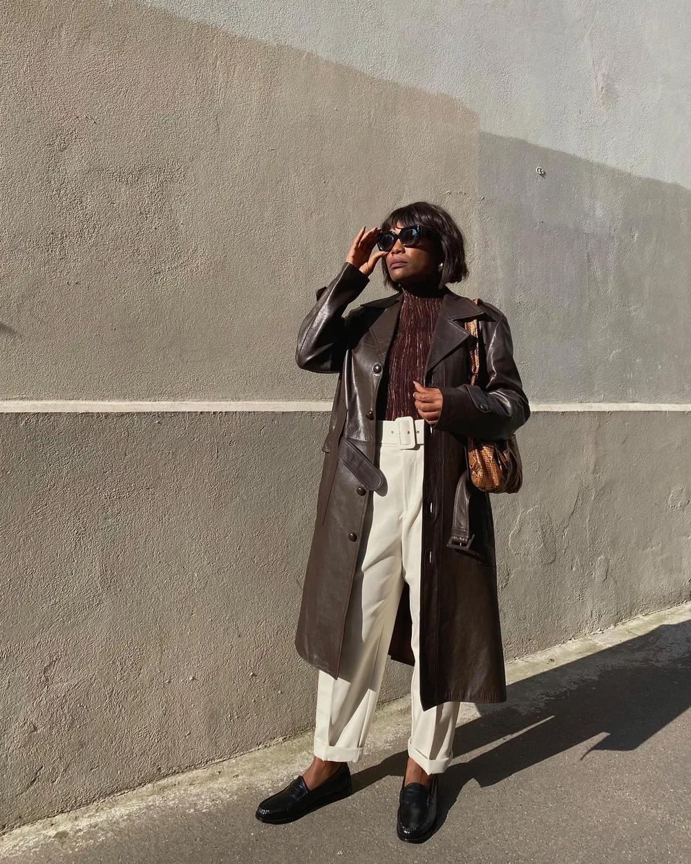 Long manteau en cuir marron porté avec un pantalon crème et des mocassins noirs