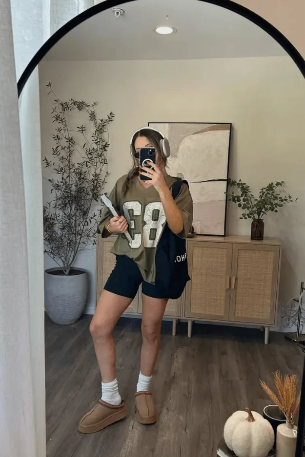 Maillot de sport oversize vert kaki floqué porté avec un short noir et des chaussons fourrés