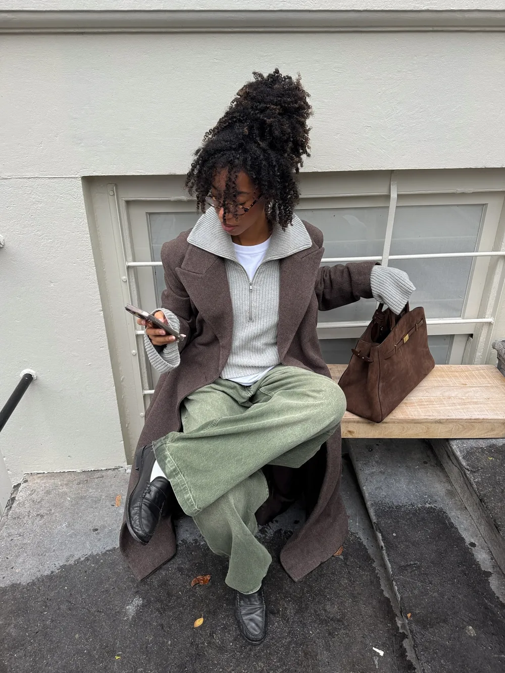 Manteau marron porté avec un pantalon vert sauge et des mocassins noirs