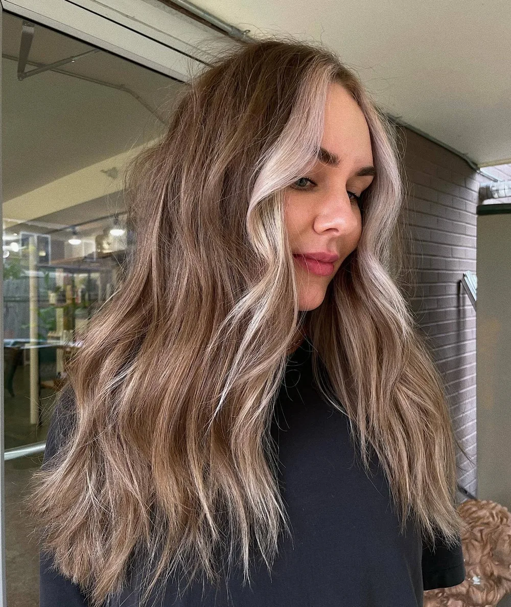 Mèches platine encadrant le visage sur cheveux bruns longs ondulés
