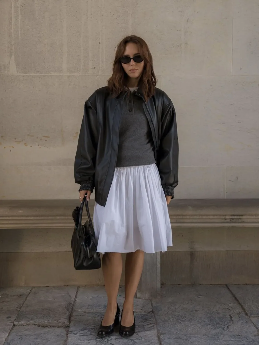 Polo en maille gris avec jupe blanche midi, bomber en cuir noir et ballerines