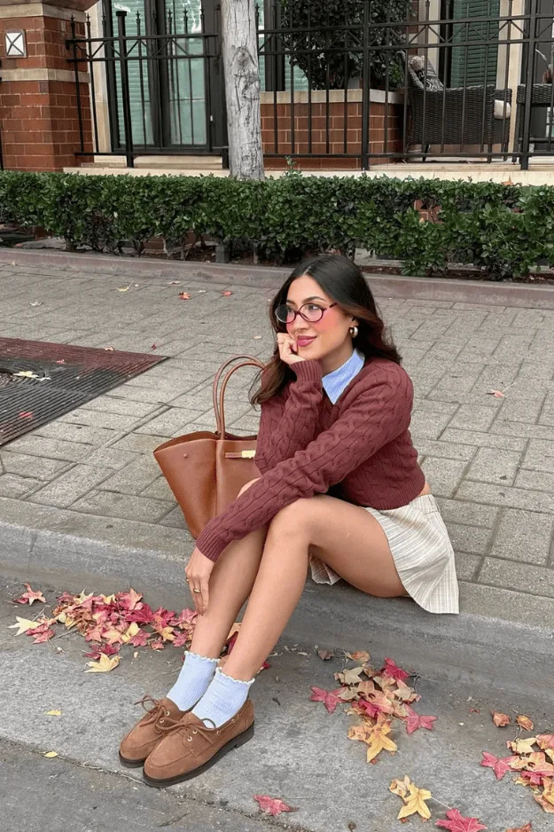 Pull bordeaux en maille torsadée porté sur une chemise avec une jupe crème et des mocassins