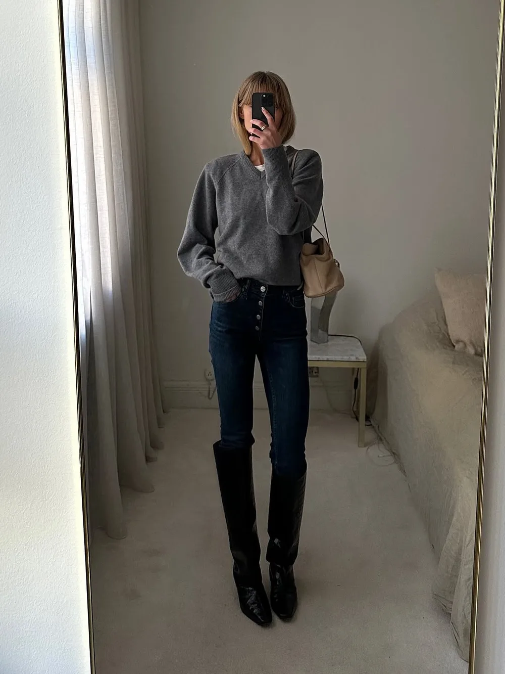 Pull gris foncé avec jean noir ajusté, bottes hautes noires et sac beige