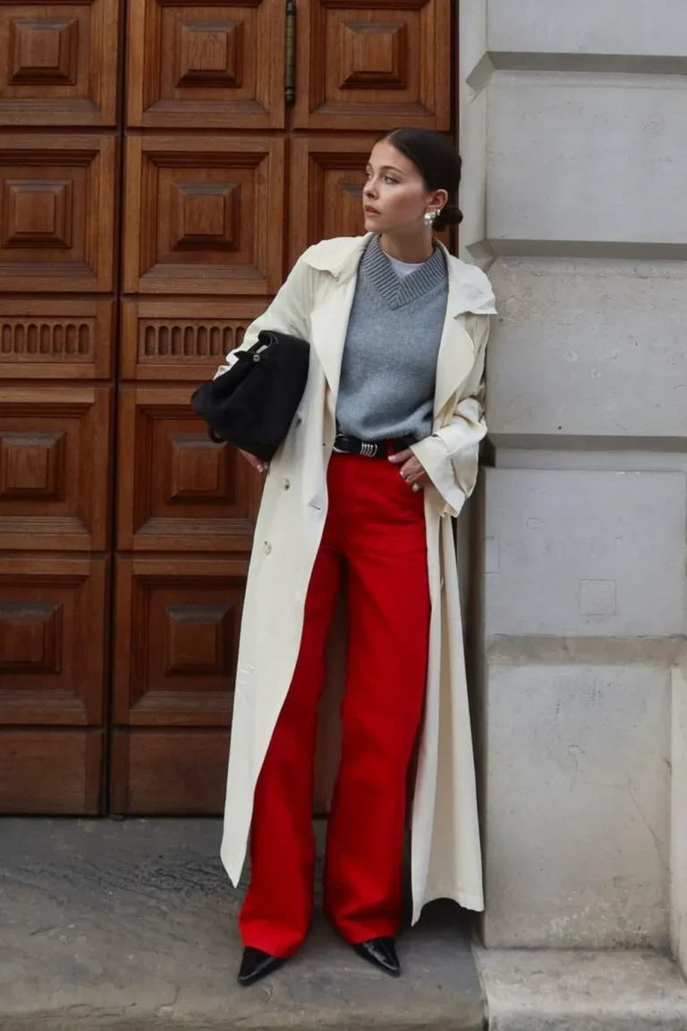 Pull gris sous un trench clair avec pantalon rouge large et bottines noires
