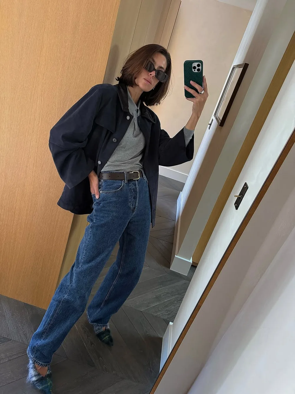 Pull gris sous une veste longue noire avec jean large et chaussures pointues