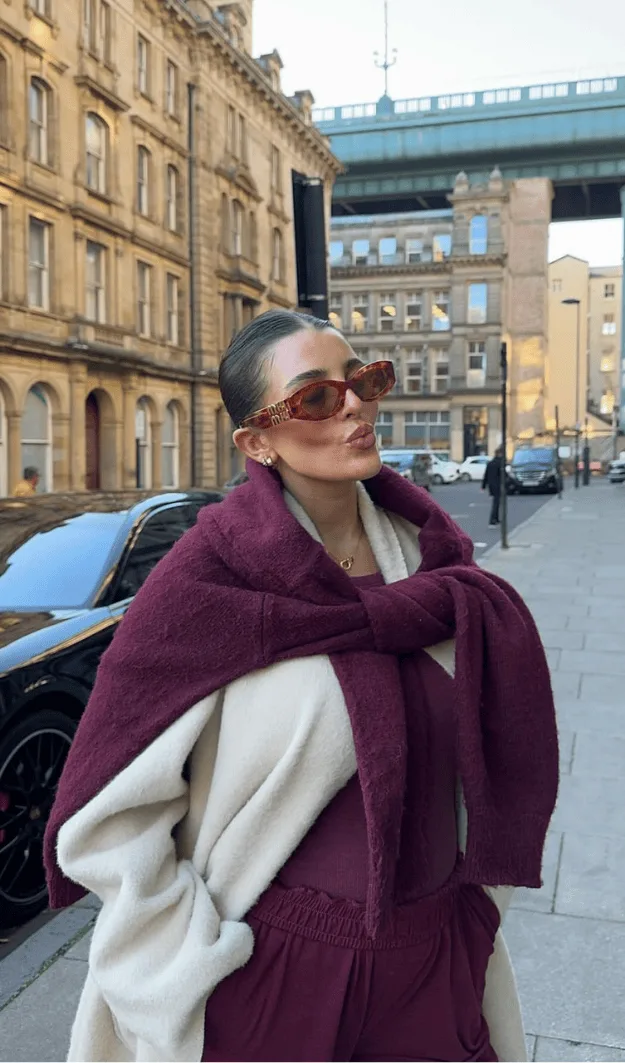 Pull prune noué sur les épaules par-dessus un manteau crème