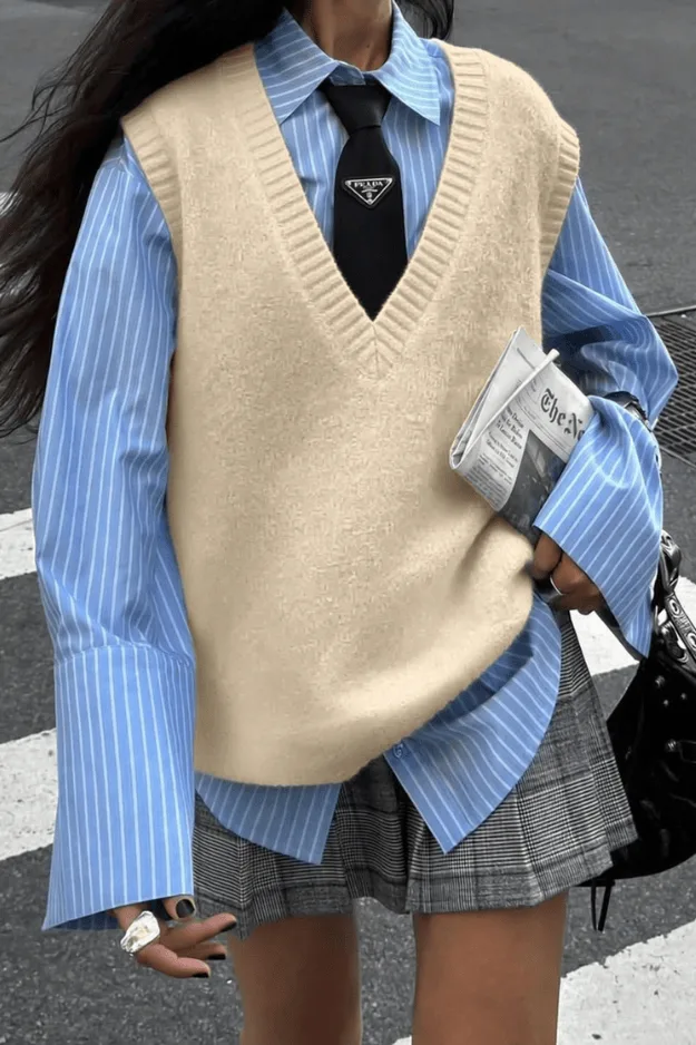 Pull sans manches crème porté sur une chemise rayée bleue et une cravate