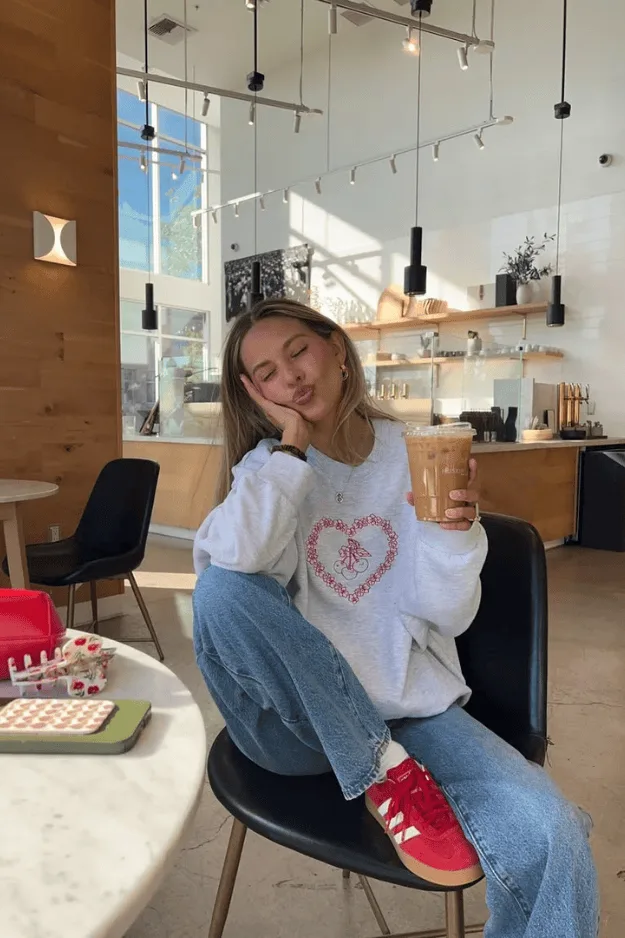 Sweat blanc à motif cœur porté avec un jean clair et des baskets rouges