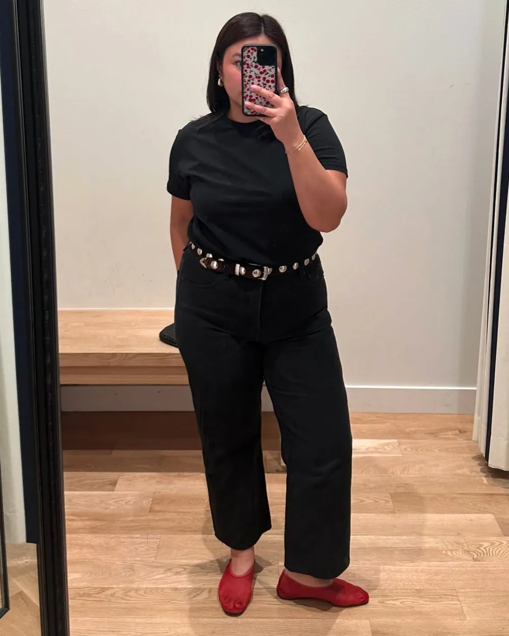 Tee-shirt noir avec jean noir court, ceinture cloutée et ballerines rouges