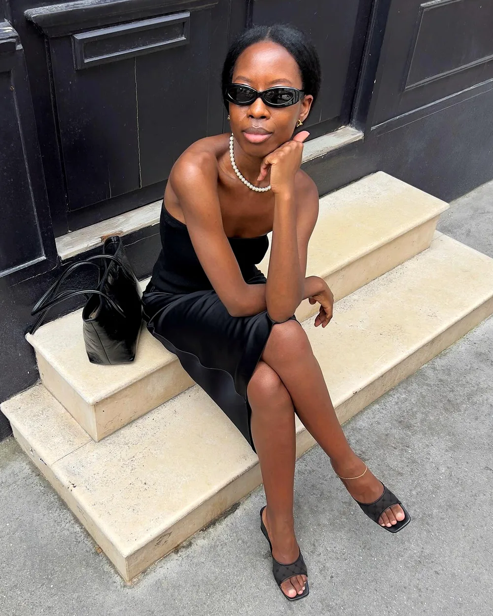 Top bandeau noir avec jupe longue satinée, mules noires et collier de perles