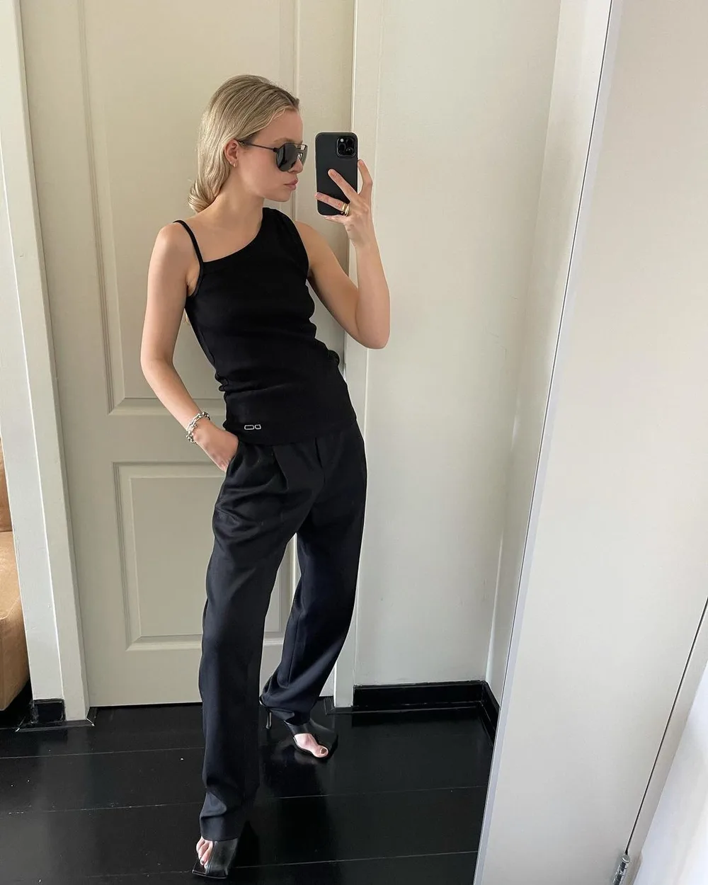Top noir asymétrique avec pantalon tailleur noir large et sandales à talons