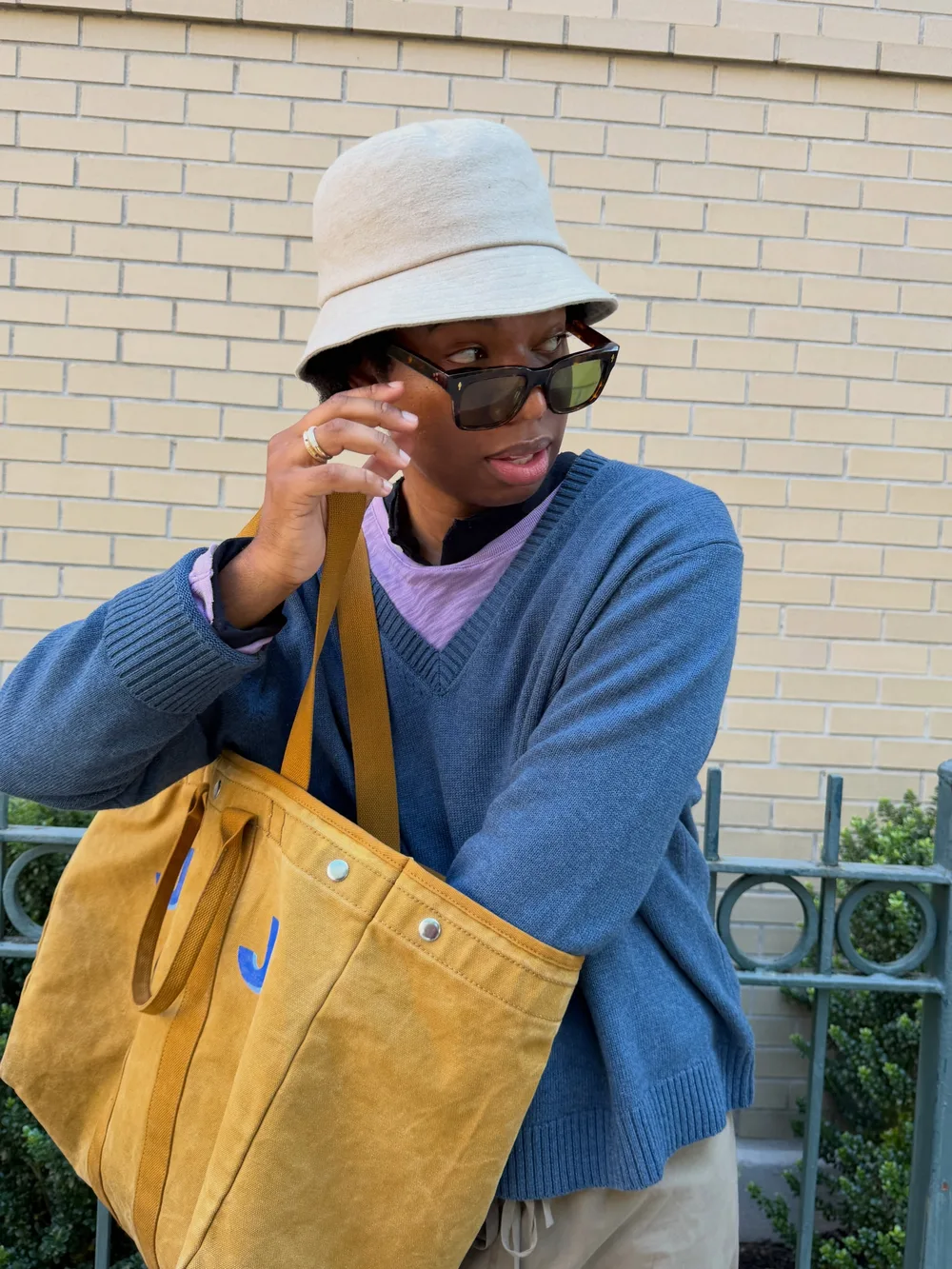 Tote bag en toile moutarde porté à l'épaule avec un pull bleu