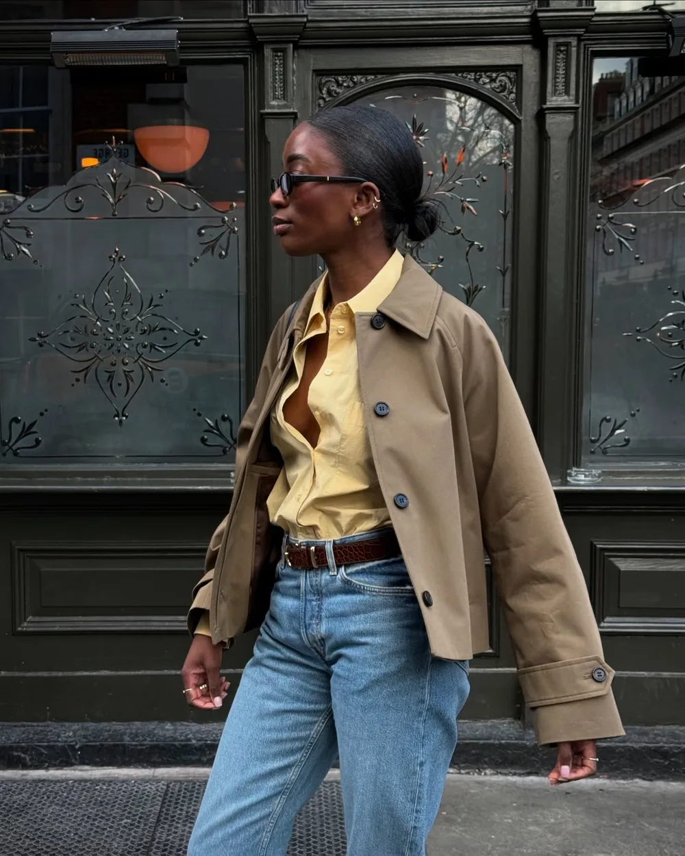 Trench court beige porté avec une chemise jaune et un jean bleu