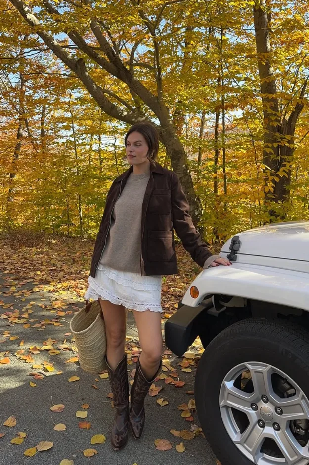 Veste en cuir marron portée avec une jupe blanche en dentelle et des santiags