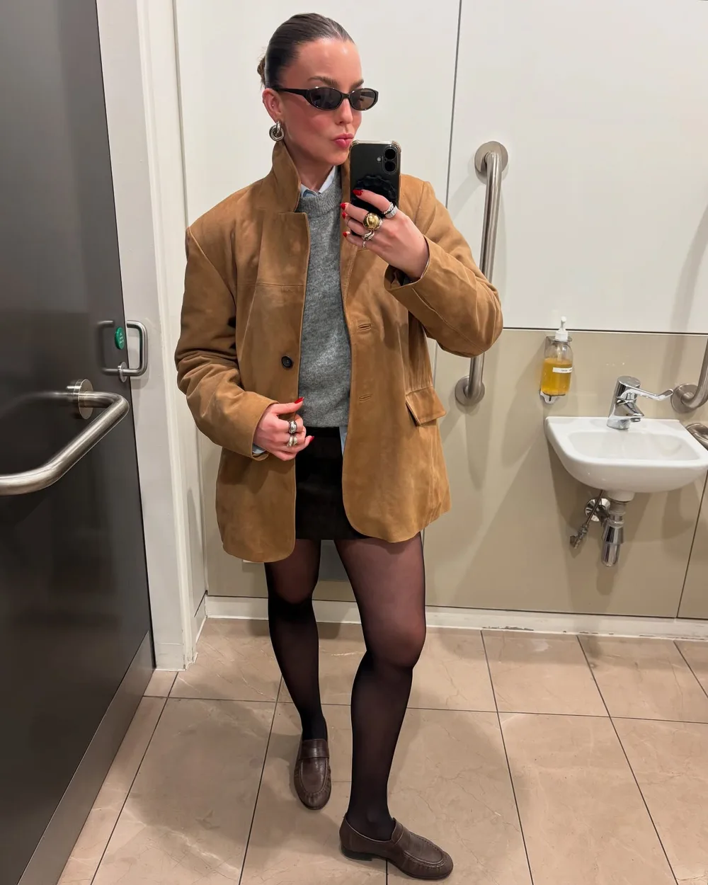 Veste en daim camel portée avec une jupe noire, des collants et des mocassins