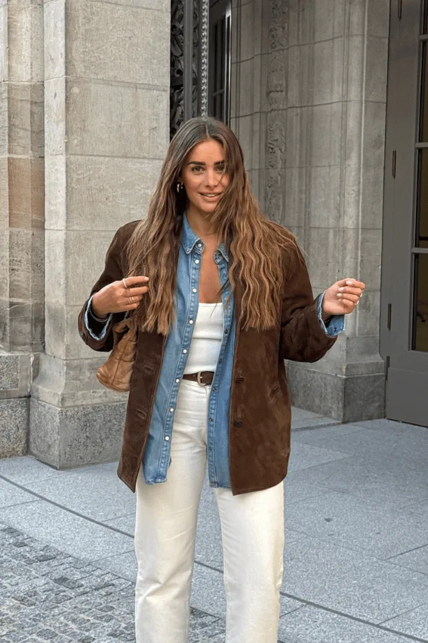Veste en daim marron portée sur une chemise en jean bleue avec un jean blanc