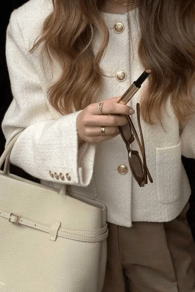 Veste en maille crème à boutons dorés portée avec un sac clair