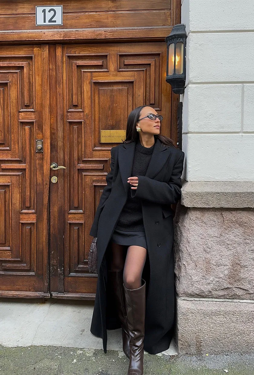 Bottes hautes marron sous mini-jupe noire avec long manteau noir