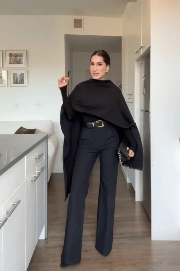 Cape noire sur pantalon sombre et ceinture fine pour un rendez-vous hivernal