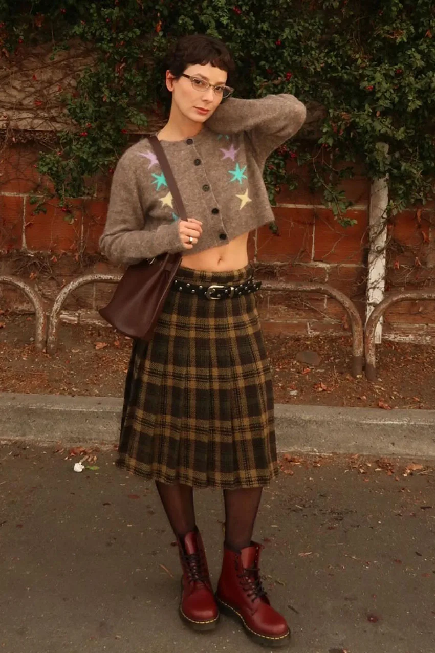 Cardigan chocolat porté avec une jupe midi tartan et des bottes rouges