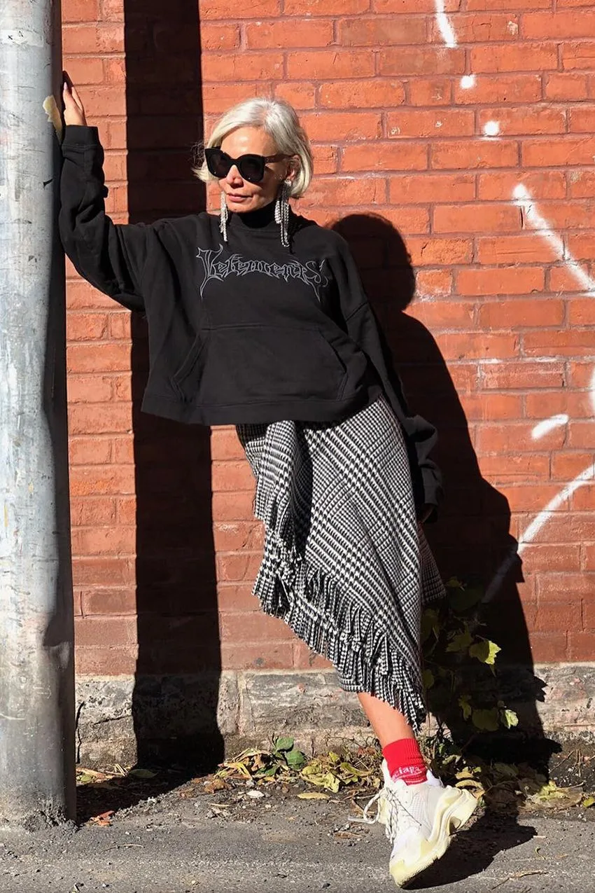 Femme aux cheveux blancs en sweat noir et jupe asymétrique à carreaux