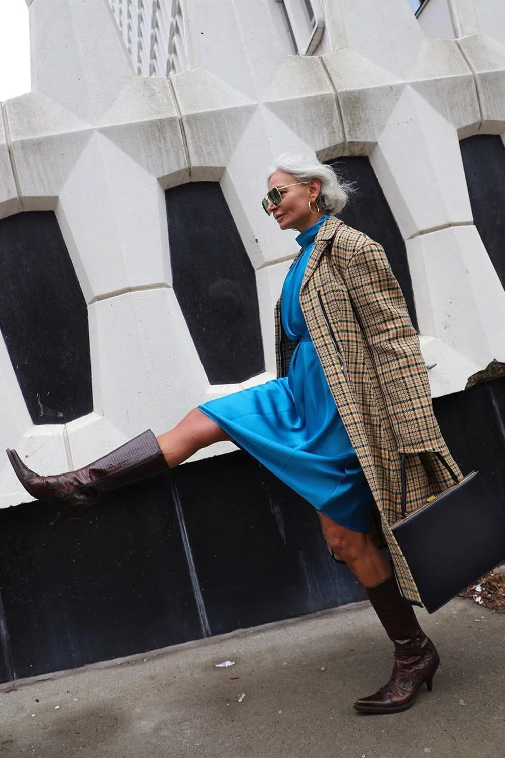 Femme de 60 ans en robe bleue avec manteau à carreaux et bottes marron