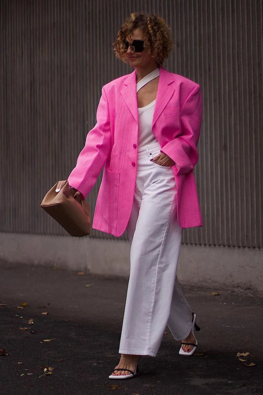 Femme de 60 ans portant un blazer fuchsia avec un pantalon blanc