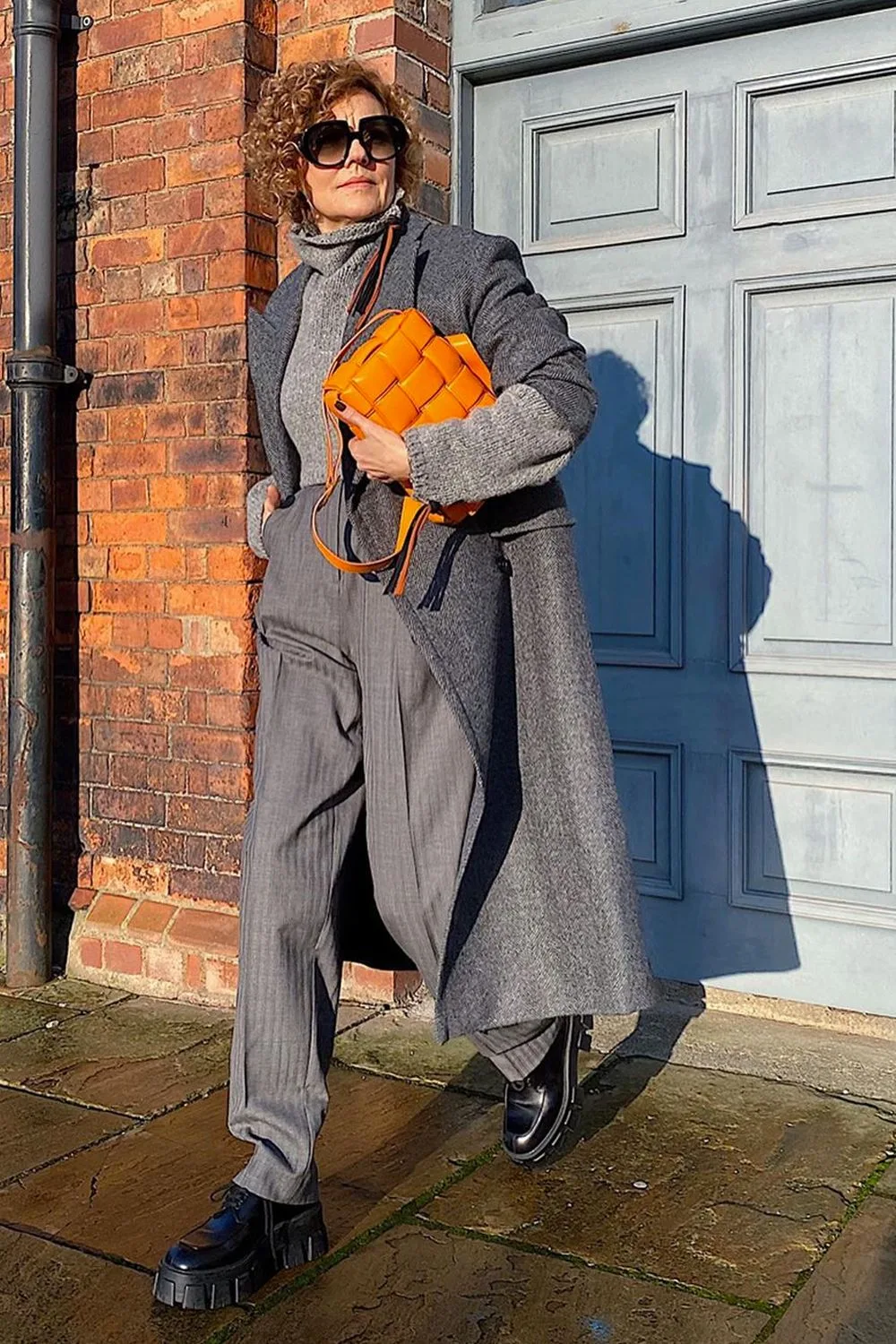 Femme de plus de 60 ans en tailleur gris ample avec sac orange