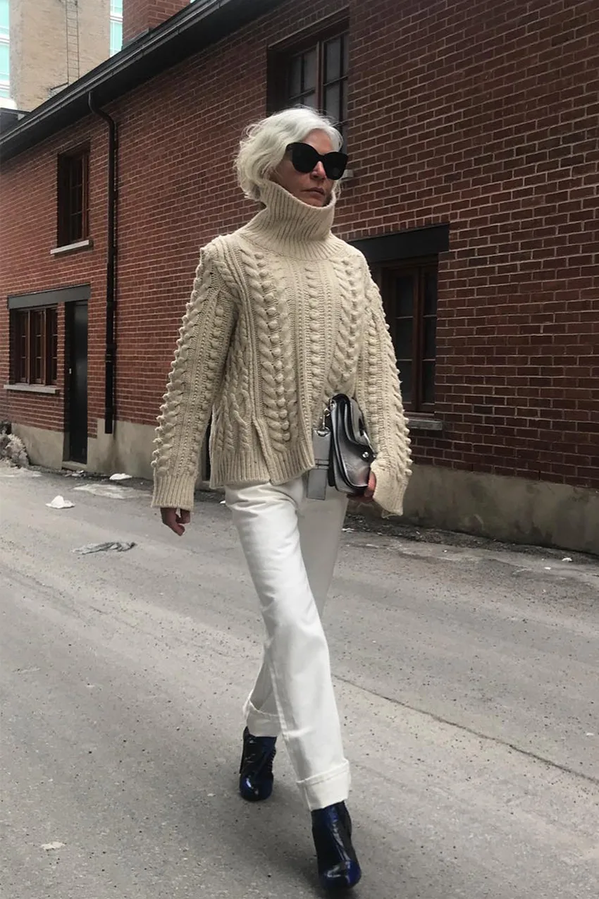 Femme mûre en jean blanc et gros pull torsadé beige