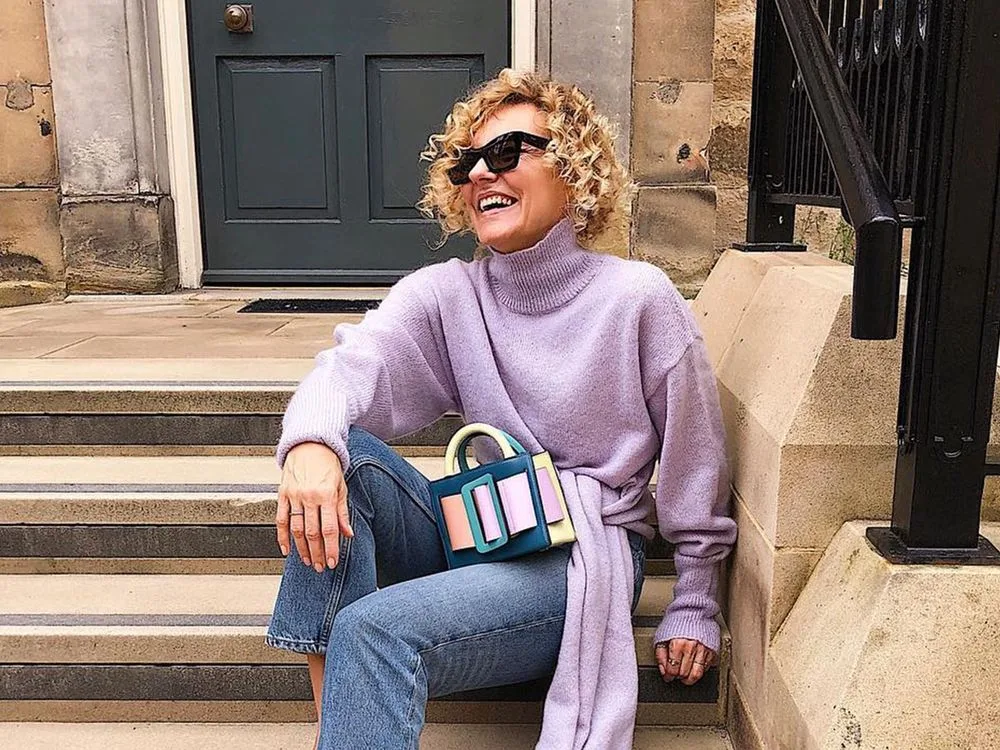 Femme mûre en pull lilas avec jean droit et sac coloré