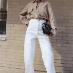 Femme mûre portant une chemise taupe avec un pantalon blanc