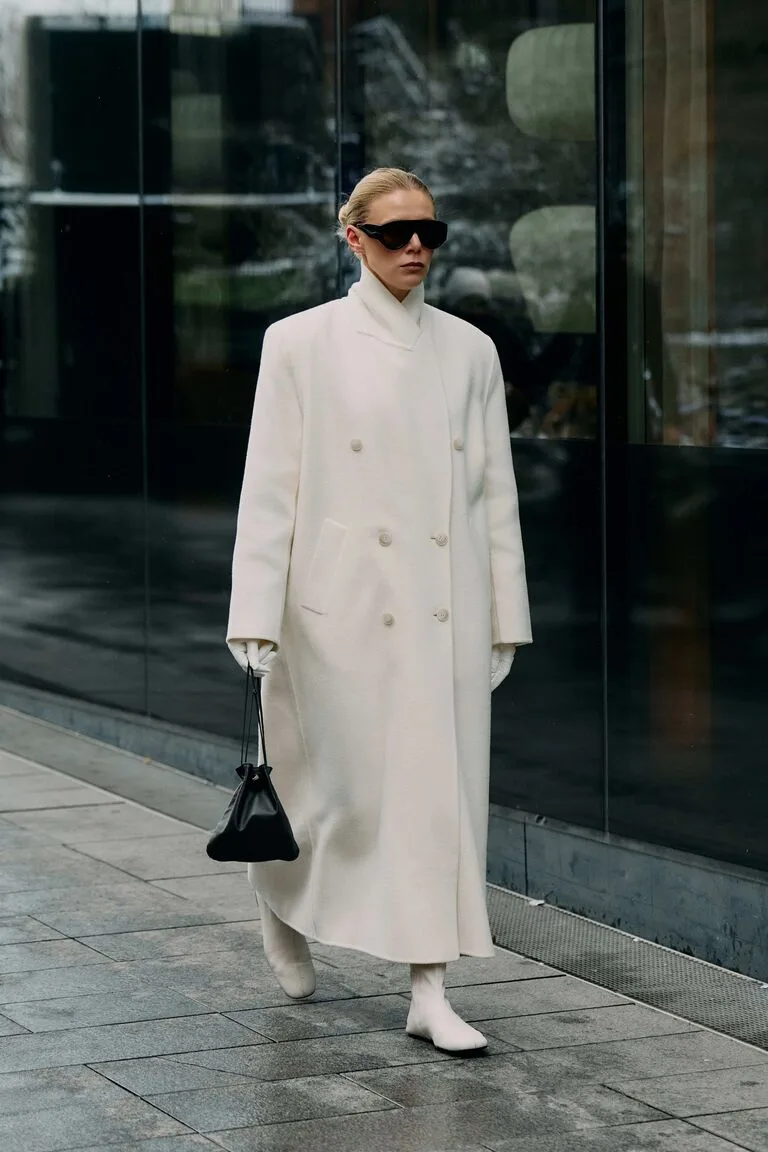 Long manteau ivoire minimaliste porté avec un sac noir