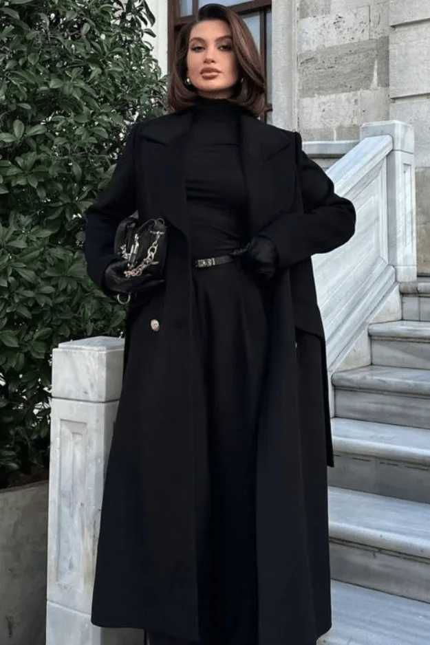 Manteau noir ample sur pantalon noir et haut noir pour un dîner chic