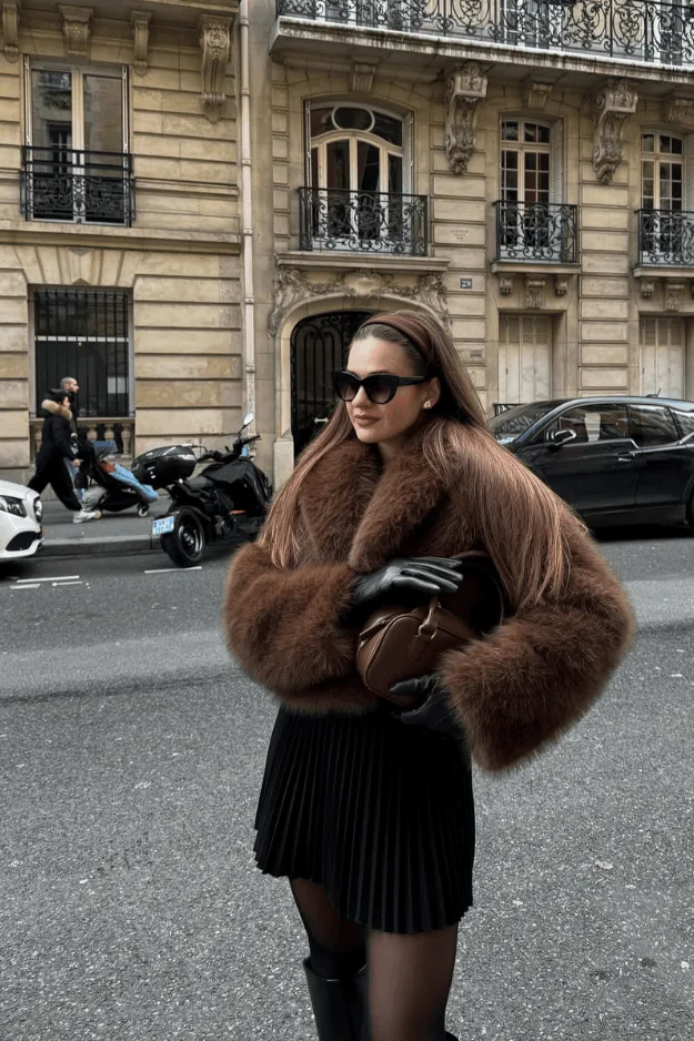 Mini-jupe noire plissée, veste brune en fausse fourrure et collants noirs