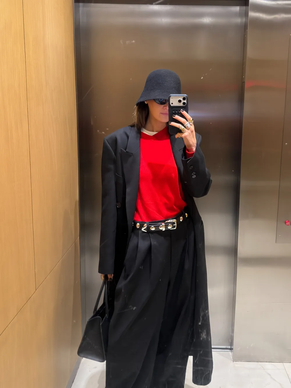 Pull rouge avec blazer noir, pantalon noir et ceinture cloutée