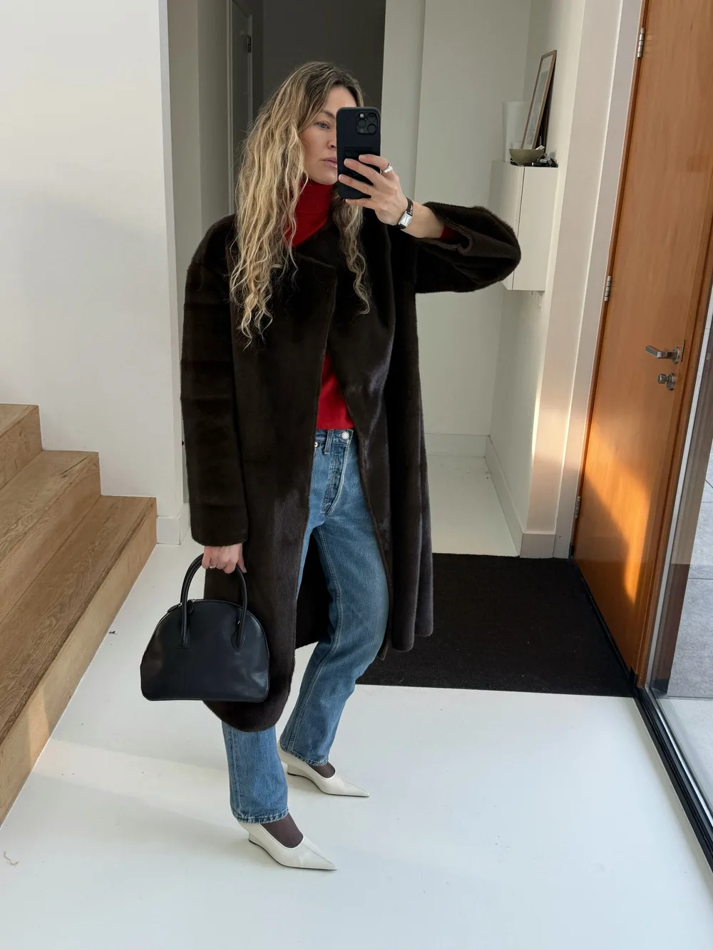 Pull rouge sous long manteau noir avec jean et chaussures claires